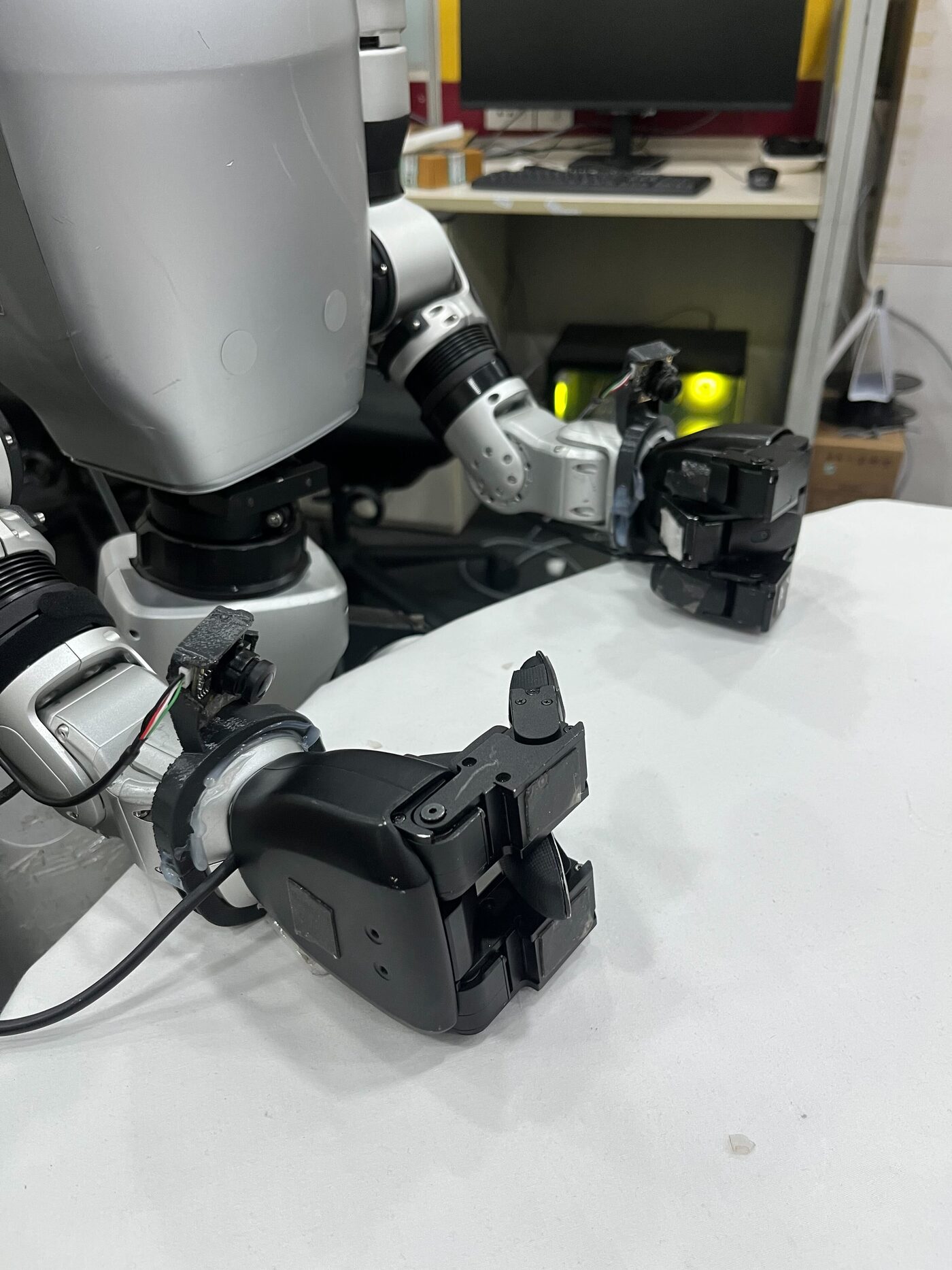 Two robot arms resting on a work surface, each ending in a multi-finger hand with a wrist-mounted camera.